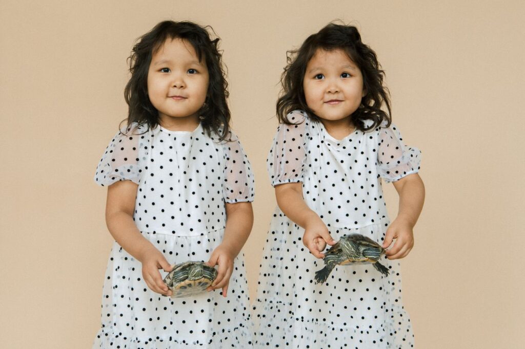 Adorable twin girls in polka dot dresses happily holding turtles in a studio setting.