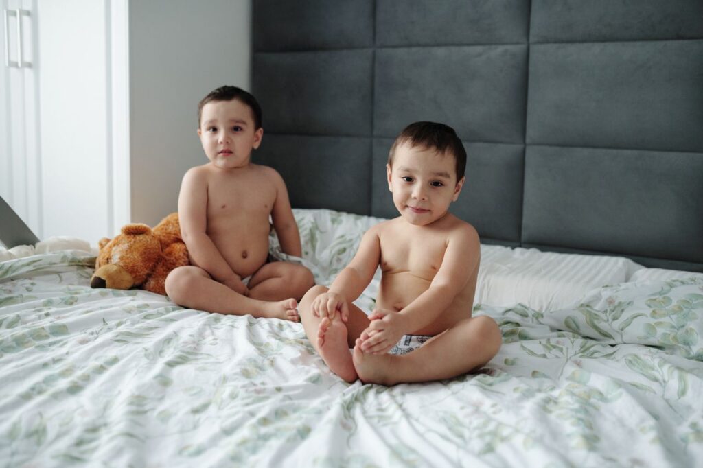 Charming image of twin brothers sitting on a bed with a teddy bear.