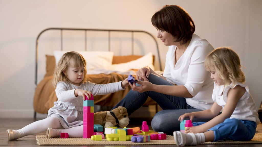 twin girl toddlers playing together with mom on the floor with blocks