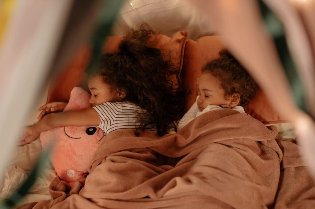 Two young children peacefully sleeping under cozy blankets, sharing a tender moment.